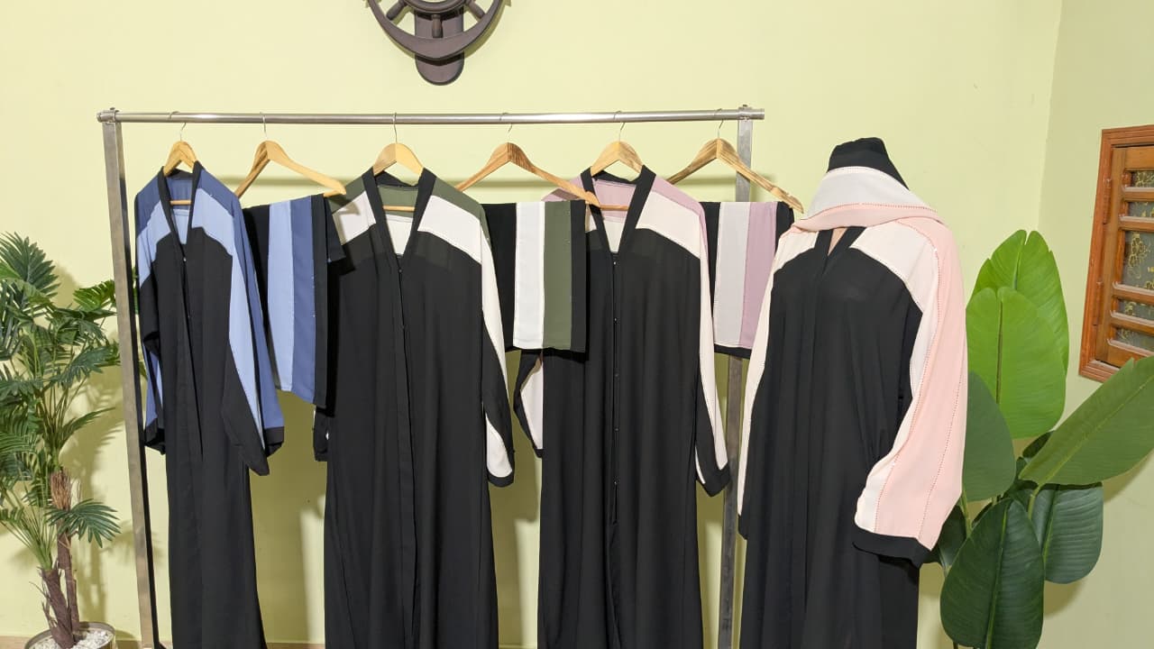 Collection of abayas on hangers against a light green wall with plants around.